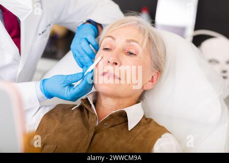 Plastic surgeon hands applying marks on face of elderly female patient Stock Photo