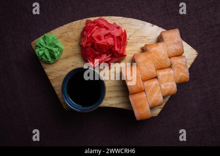 Closeup of traditional Japanese sushi rolls, wasabi paste, and pickled ginger on a wooden plate over dark background Stock Photo