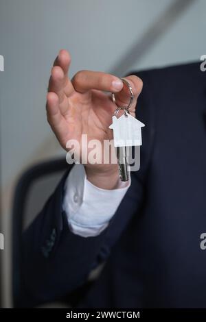 The image shows a persons hand holding a silver house key with a house-shaped keychain. The key is isolated on a white background. Stock Photo