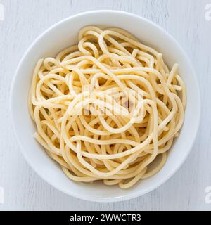 Cooked spaghetti in a white ceramic bowl isolated on white painted wood. Top view. Stock Photo