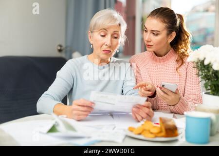 Elderly woman with adult daughter using smartphone and checking utility bills Stock Photo