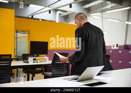 Young male manager leaning on table while reading paper document Stock Photo