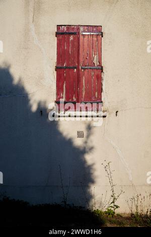 Peeling Red Paint on Window Shutter with Large Shadow on Wall Stock Photo