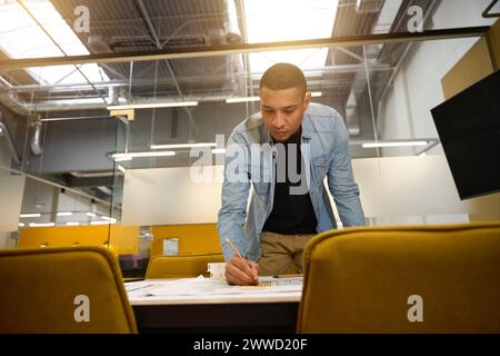 Serious young man leaning over table and writing something Stock Photo