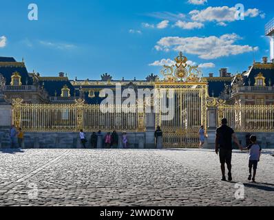 Versailles,Paris,France,June 30, 2022. People in the shadow of the magnificent golden gate of the royal palace. The late afternoon light enhances its Stock Photo