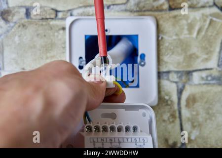 Connecting wires to wall thermostat for floor heating system, an electrician uses crosshead screwdriver for installation. Stock Photo
