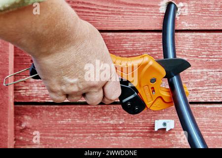 Using ratchet shears to cut HDPE pipes when installing an external drinking water supply. Stock Photo