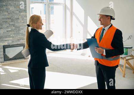 Woman and foreman standing in room and shaking hands Stock Photo