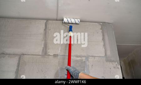 Worker using paint roller to paint the wall. Prime the wall using a long roller. White emulsion paint on the wall with a roller. some improvements. Stock Photo