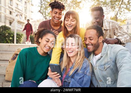 Diverse group university friends sitting on stairs in street city. Happy students using smartphones. Stock Photo