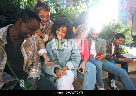 Diverse group university friends sitting on stairs in street city. Happy students using smartphones. Stock Photo