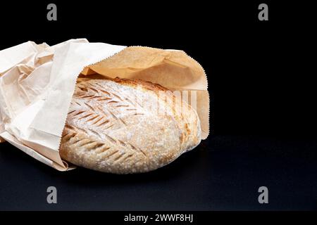 Freshly baked Vermont rye bread with crisp crust and porous texture in flour and bemag bag on black background. Freshly baked homemade bread Stock Photo