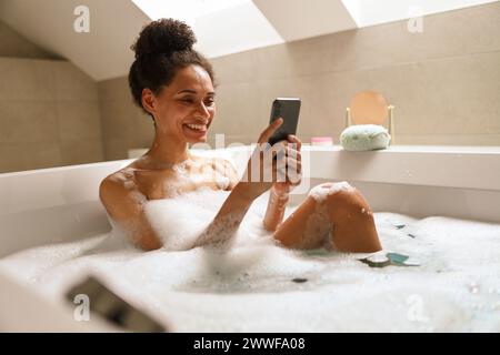 a woman is sitting in a bathtub using a cell phone Stock Photo