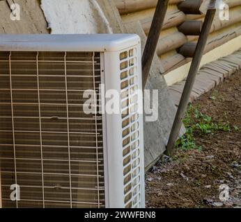 Closeup of air conditioner condenser unit on ground with exterior wall of log cabin in background in South Korea Stock Photo