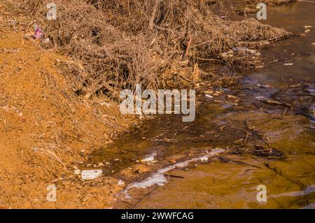A small stream flows through a muddy landscape with signs of vegetation erosion, in South Korea Stock Photo