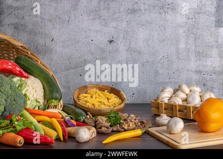 Various fresh vegetables such as peppers, cauliflower, peppers, mushrooms and broccoli around and in a basket with a bowl of pasta next to it on a Stock Photo