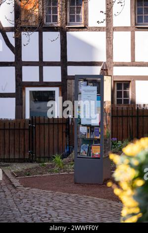 Bookcase in front of half-timbered house and fence, many colourful books in a glass display case, outdoor, cobblestone pavement, in the foreground on Stock Photo