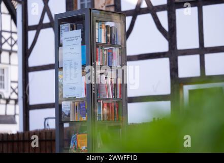 Open bookcase in front of half-timbered house and fence, many colourful books in a glass display case, outdoors, in the foreground on the right, a Stock Photo