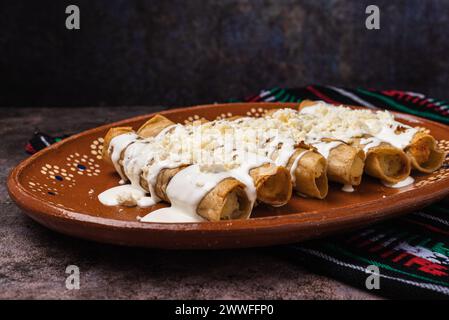 Fried potato tacos with cream and cheese in a Mexican mud dish. Tacos dorados, Mexican food. Stock Photo