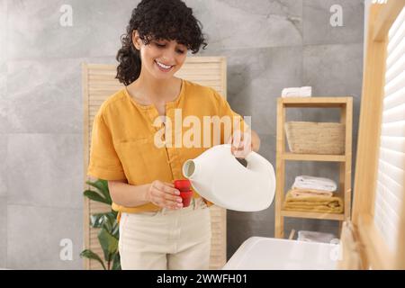 Happy woman pouring laundry detergent into cap indoors Stock Photo