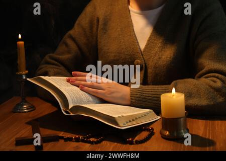Woman reading Bible at table with burning candles, closeup Stock Photo