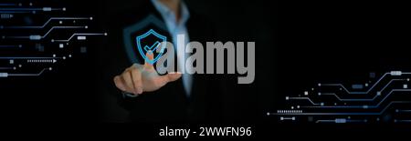 A blue circuit board with a metallic shield on it with a digital screen interface and a businessman dressed in black suit pointing finger in backgroun Stock Photo