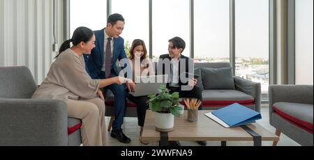 A group of business professional gathered around a small table in a modern office setting with large window that let in natural light. Young woman eng Stock Photo