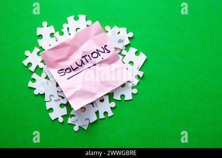 Pink crumpled paper with solutions written on it resting on white jigsaw puzzle pieces Stock Photo