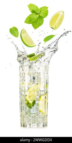 Lime wedges and mint leaves falling into an overflowing glass of mojito cocktail isolated on white background. Stock Photo