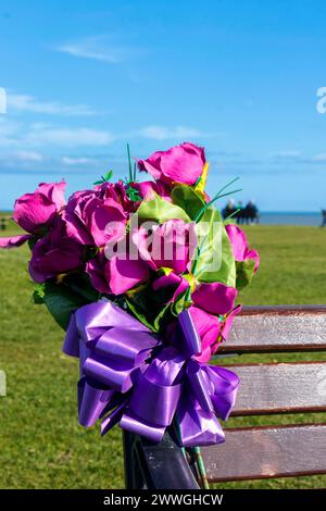 closeup artificial memorial flowers left by relative on bench by the sea Newbiggin by Sea, Northumberland, England uk Stock Photo
