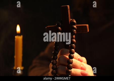 Woman with cross, beads and burning candle praying on blurred background, closeup Stock Photo