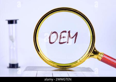 OEM original equipment manufacturer concept. Text through a magnifying glass on a gray background next to an hourglass Stock Photo