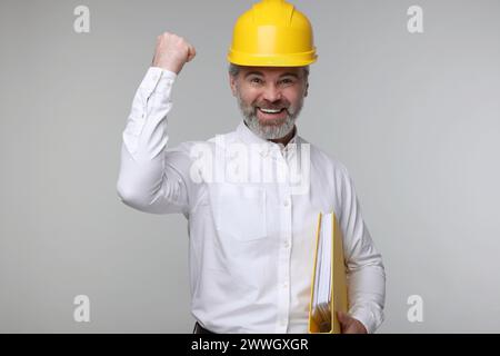 Architect in hard hat holding folder on grey background Stock Photo
