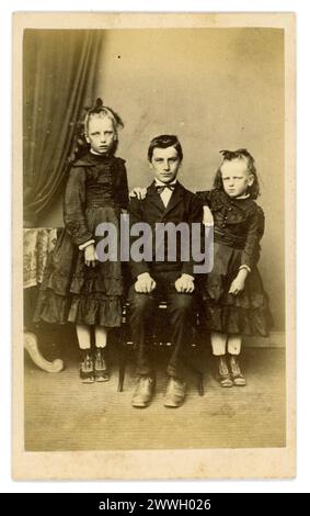Original Victorian carte de visite (CDV or visiting card) older arrogant looking boy with his young sisters, scary, spooky looking Victorian children. Studio of John Shield, Allendale Town, Northumberland, circa 1860's from card mount. Stock Photo