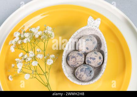 Creative plate with bunnies ears with quail eggs and white Gypsophila twig on yellow and white plates close up. Holiday table setting. Idea of elegant Stock Photo