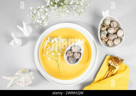 Easter table serving arrangement. Holiday elegant table setting idea in white yellow tones. Stylish tableware, napkin, quail eggs, gold cutlery, sprin Stock Photo