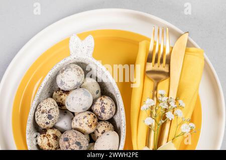 Close up Easter table setting in white yellow colors with beautiful dishware, quail eggs of natural colors, golden cutlery. Holiday table setting. Hor Stock Photo