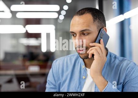 A focused young businessman engaged in a phone conversation in a modern office environment. Stock Photo