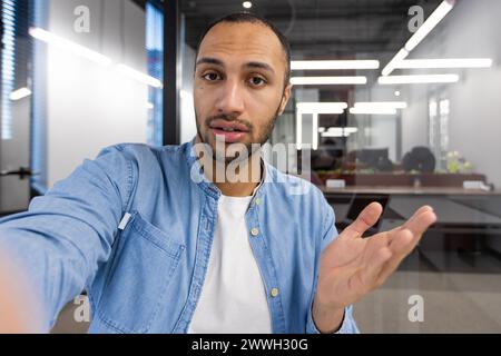 A man with a beard and a blue shirt is looking at the camera. He is wearing a white shirt underneath the blue shirt Stock Photo