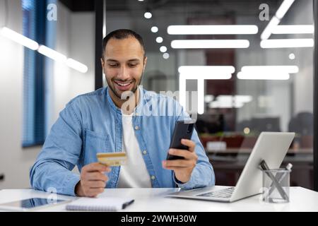 A man is smiling while using his cell phone to pay for something with a credit card. Concept of convenience and ease in making transactions using technology Stock Photo