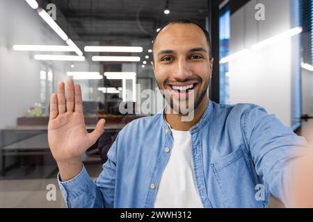 A man with a big smile on his face is waving at the camera. He is wearing a blue shirt and white shirt Stock Photo