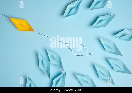 Group of blue paper boats and one red with paths on a blue background. Concept of a strong leader with extraordinary thi Group of blue paper boats and Stock Photo