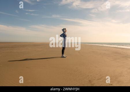 Rear view of a sporty woman with her hands on her hips resting after exercise at the beach, getting away from it all Stock Photo