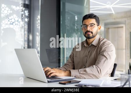 Professional Indian businessman in a modern office working intently on a laptop, portraying confidence and dedication. Stock Photo