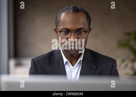 Serious focused male businessman working inside office with laptop, mature experienced african american man typing on keyboard, thinking reading from monitor. Stock Photo