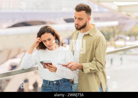 Travel Issue. Stressed young couple looking at smartphone while standing in airport Stock Photo