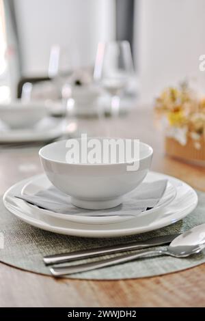 Close up white porcelain tableware plates on place mats and empty wine glasses ready for dinner. Table settings wait for guests at home or restaurant. Stock Photo