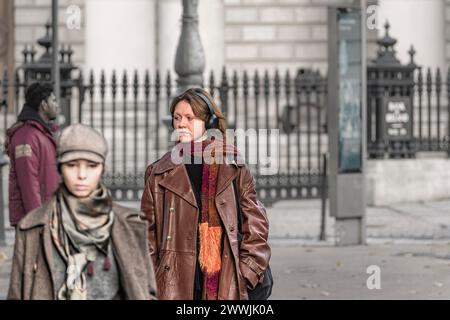 Street portrait of a relaxed young happy stylish woman in headphones wearing brown colours walking towards the camera. Dublin. Ireland. Stock Photo