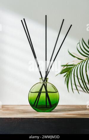 Aromatic Reed Diffuser on Wooden Table With Vibrant Green Leaves Against White Background Stock Photo