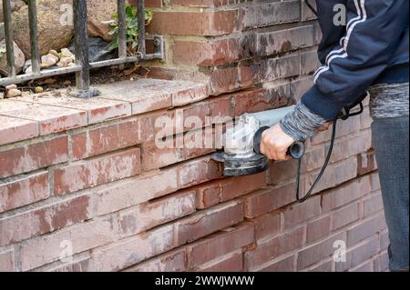 Repairing broken brick wall. Women cleaning grouts with a grinder. Stock Photo